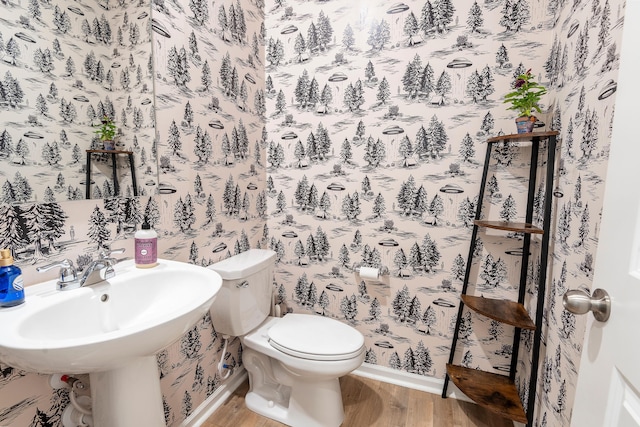 bathroom featuring wood finished floors, toilet, wallpapered walls, baseboards, and a sink