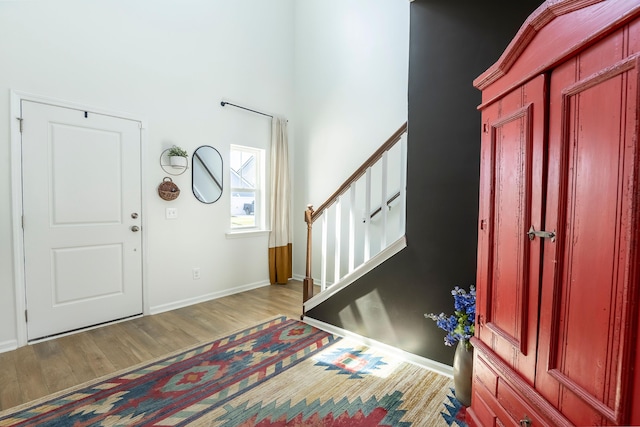 foyer entrance with stairway, wood finished floors, a high ceiling, and baseboards