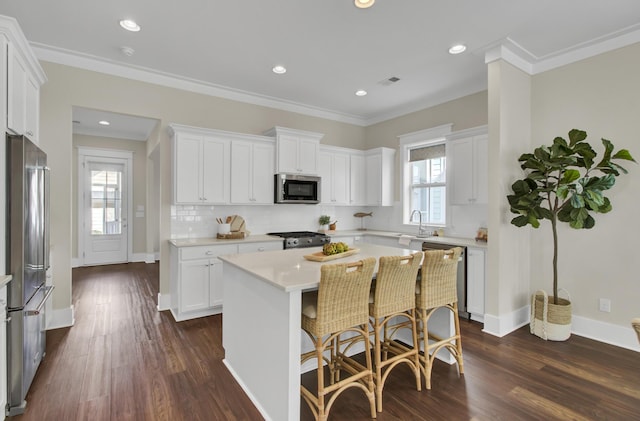 kitchen with white cabinets, appliances with stainless steel finishes, crown molding, and a center island