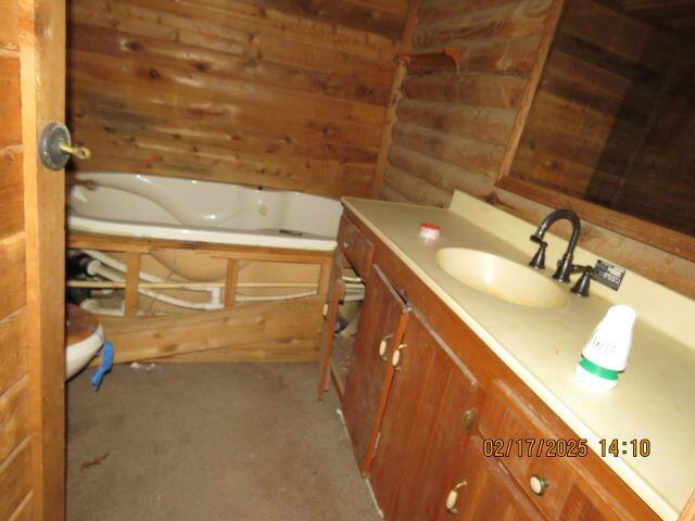 bathroom with rustic walls, vanity, and a bath