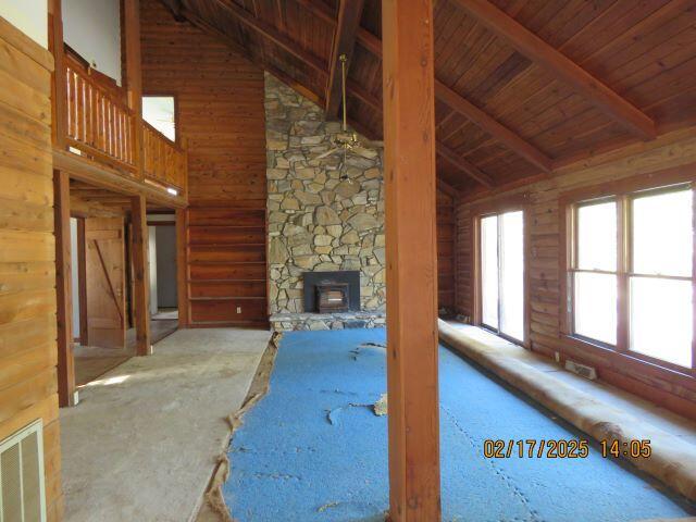 unfurnished living room with log walls, beamed ceiling, high vaulted ceiling, and wooden ceiling