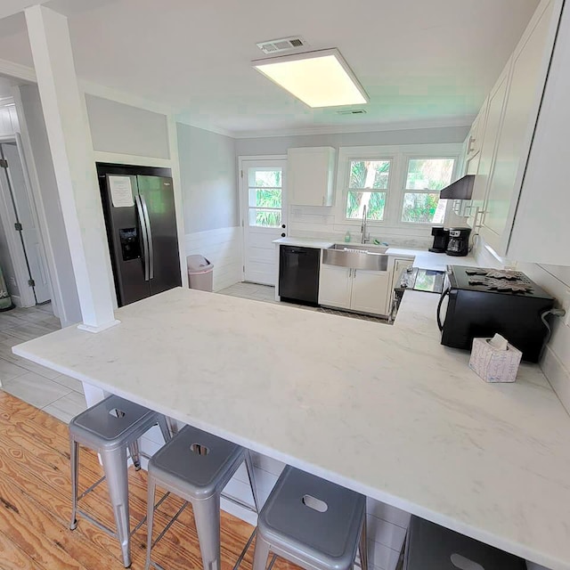 kitchen featuring a kitchen breakfast bar, stainless steel fridge, kitchen peninsula, dishwasher, and white cabinets