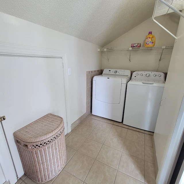 clothes washing area with a textured ceiling, washing machine and clothes dryer, and light tile patterned flooring