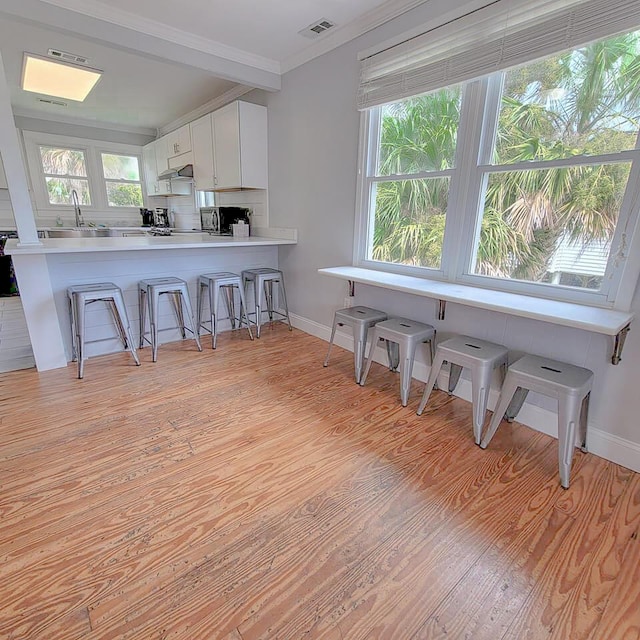 kitchen with a breakfast bar, white cabinetry, tasteful backsplash, light hardwood / wood-style floors, and kitchen peninsula