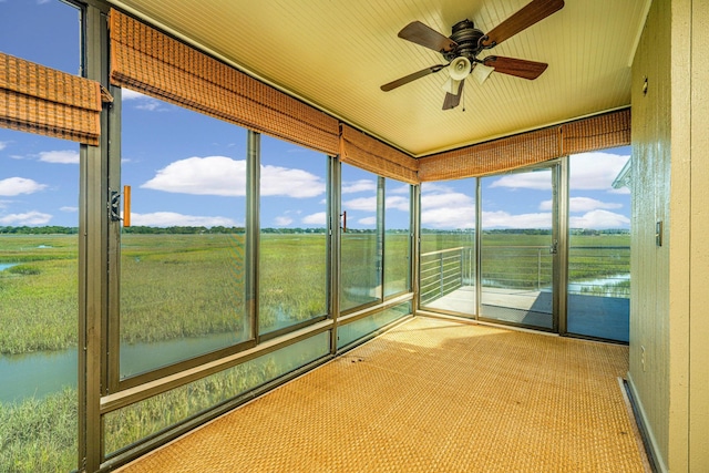 unfurnished sunroom with ceiling fan, a rural view, and a water view