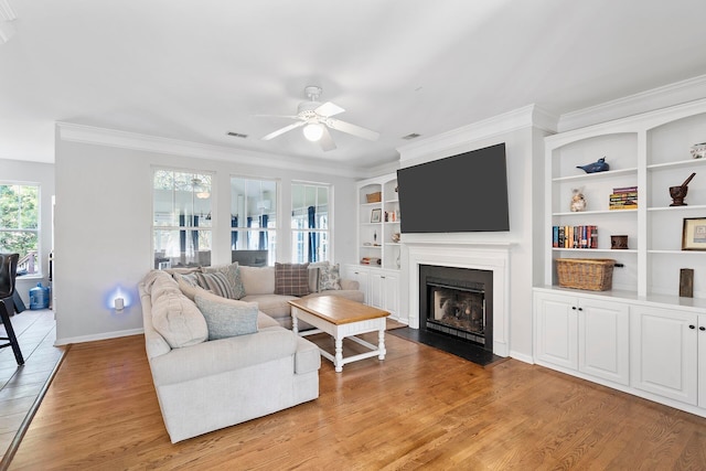 living room with built in features, light hardwood / wood-style floors, ceiling fan, and crown molding