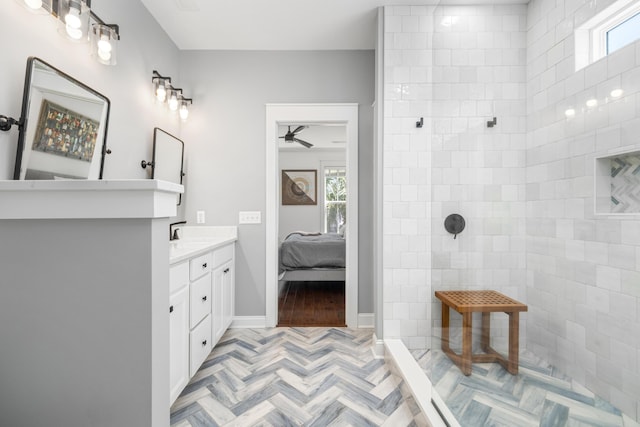 bathroom with a ceiling fan, vanity, baseboards, tiled shower, and ensuite bathroom