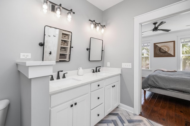 ensuite bathroom with ceiling fan, baseboards, a sink, and double vanity