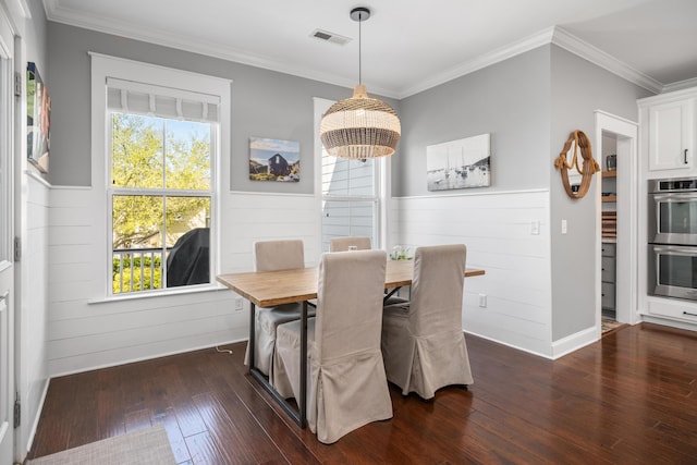 dining area featuring dark wood-type flooring, crown molding, plenty of natural light, and a wainscoted wall