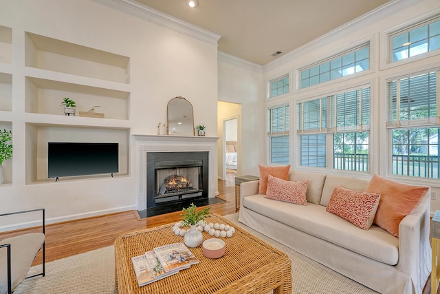 living area with ornamental molding, a fireplace with flush hearth, wood finished floors, and a healthy amount of sunlight