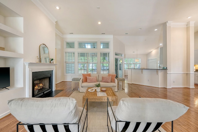 living room featuring baseboards, light wood finished floors, a warm lit fireplace, ornamental molding, and recessed lighting
