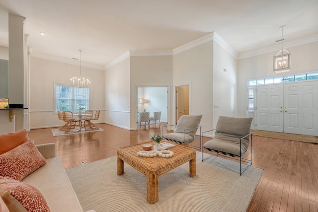 living area featuring a towering ceiling, baseboards, an inviting chandelier, ornamental molding, and hardwood / wood-style floors