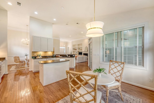 kitchen featuring a kitchen island, visible vents, crown molding, white cabinets, and light wood finished floors