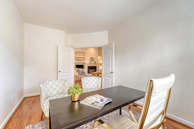 dining room featuring baseboards, light wood-style floors, and a fireplace