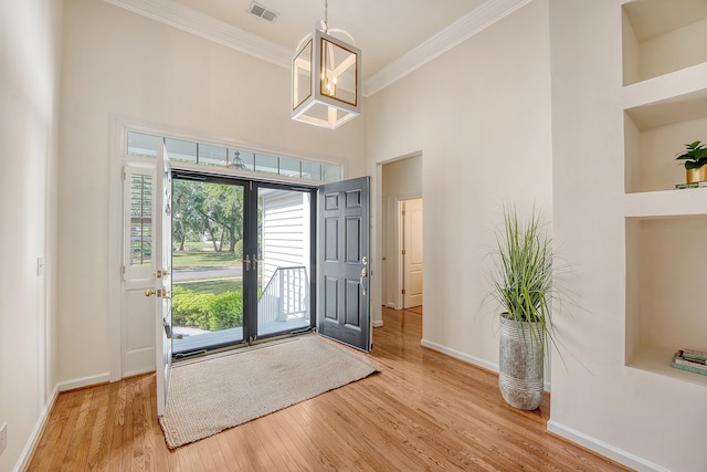 foyer featuring visible vents, ornamental molding, baseboards, and a high ceiling