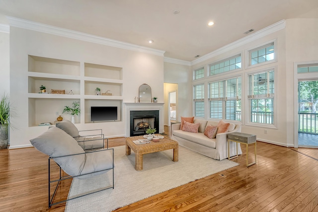 living room with crown molding, visible vents, built in features, baseboards, and light wood-style flooring