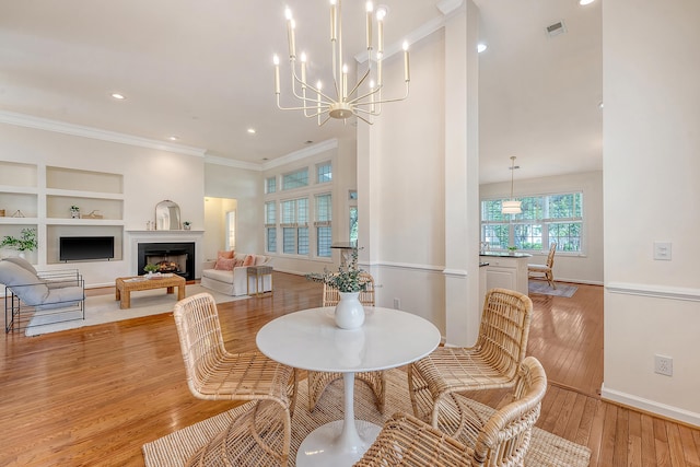 dining area featuring visible vents, crown molding, a fireplace, light wood-type flooring, and built in shelves