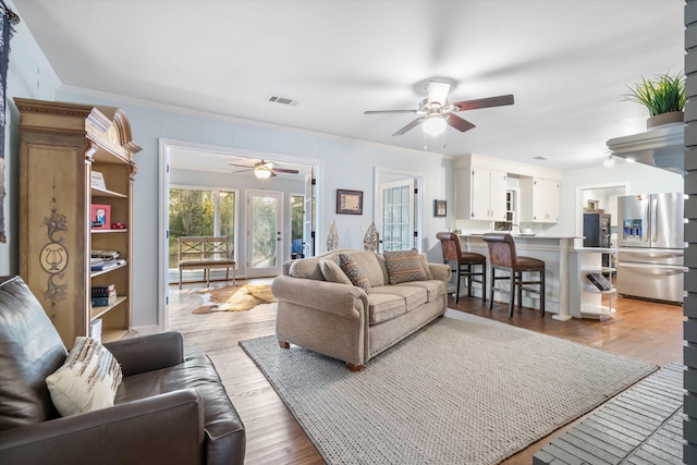 living room featuring a ceiling fan, visible vents, and light wood finished floors