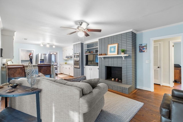 living area with a ceiling fan, ornamental molding, a brick fireplace, wood finished floors, and baseboards