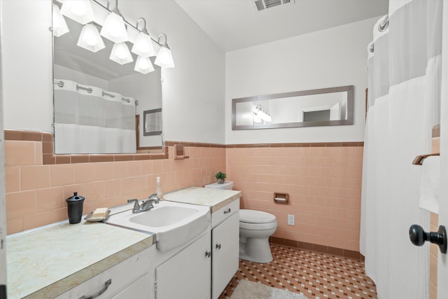 full bathroom with wainscoting, toilet, tile patterned floors, vanity, and tile walls