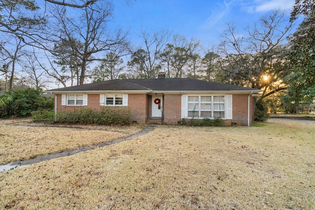 ranch-style home featuring brick siding, a chimney, and a front yard