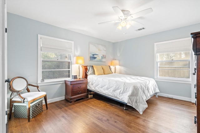 bedroom with multiple windows, wood finished floors, visible vents, and baseboards