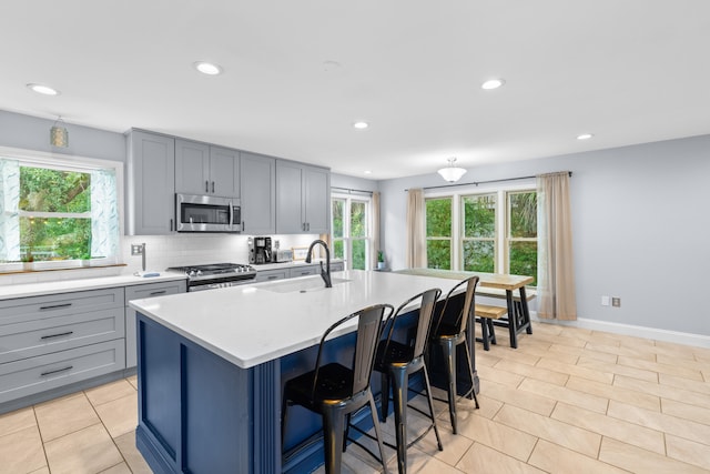 kitchen with appliances with stainless steel finishes, sink, an island with sink, a breakfast bar area, and decorative backsplash