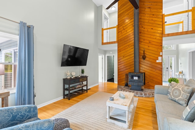 living room featuring a healthy amount of sunlight, light hardwood / wood-style flooring, a high ceiling, and a wood stove