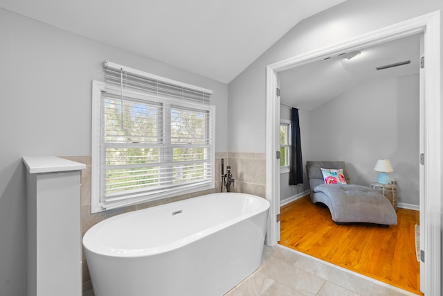 bathroom with a healthy amount of sunlight, vaulted ceiling, a bath, and wood-type flooring