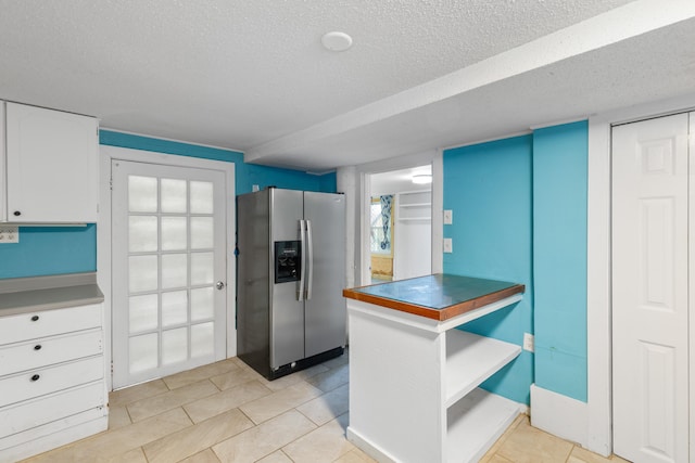 kitchen featuring a textured ceiling, stainless steel fridge, white cabinetry, and light tile patterned flooring