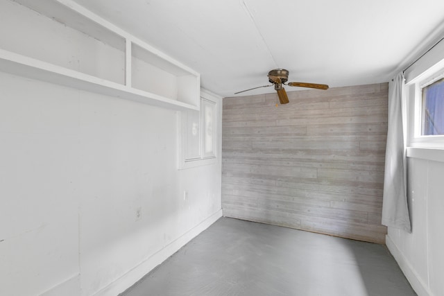 unfurnished room featuring concrete flooring, ceiling fan, and wood walls