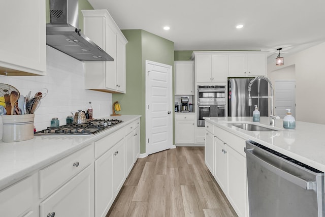 kitchen with appliances with stainless steel finishes, wall chimney exhaust hood, tasteful backsplash, light wood-style floors, and light countertops