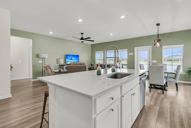 kitchen featuring a sink, an island with sink, light wood-style flooring, white cabinets, and hanging light fixtures