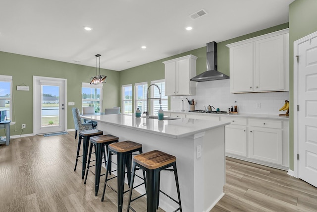kitchen with wall chimney exhaust hood, a sink, a center island with sink, a breakfast bar, and decorative backsplash