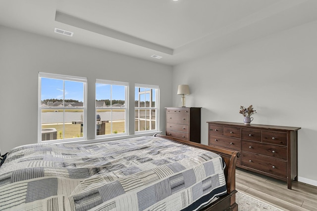 bedroom featuring light wood finished floors, baseboards, and a raised ceiling