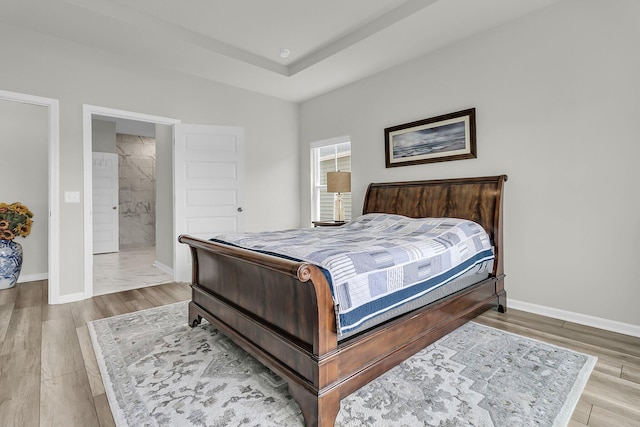 bedroom featuring wood finished floors, baseboards, and ensuite bathroom