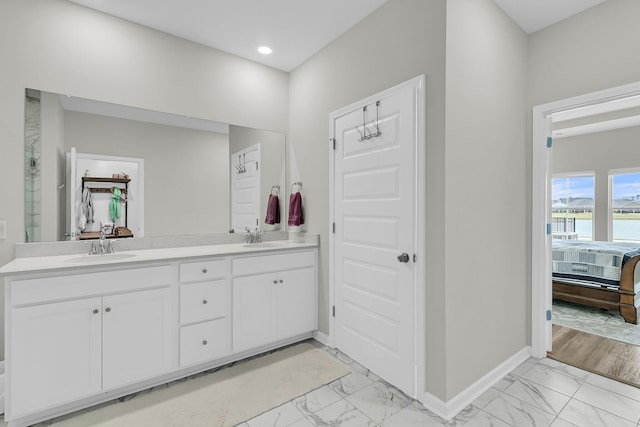 ensuite bathroom featuring marble look tile flooring, baseboards, double vanity, and recessed lighting