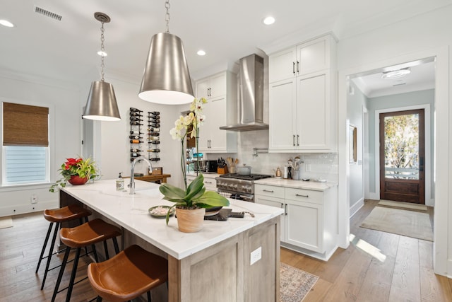 kitchen featuring wall chimney exhaust hood, white cabinetry, an island with sink, and high end range