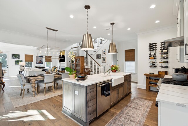 kitchen featuring dishwasher, sink, an island with sink, decorative light fixtures, and light wood-type flooring