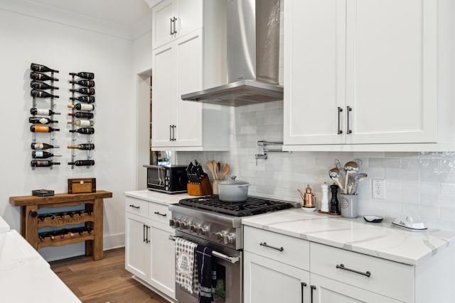 kitchen with wall chimney range hood, hardwood / wood-style flooring, light stone countertops, high end stove, and white cabinetry