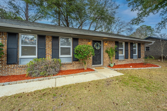 ranch-style home with brick siding, a front lawn, and roof with shingles