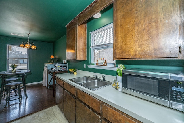 kitchen with a sink, baseboards, light countertops, an inviting chandelier, and pendant lighting