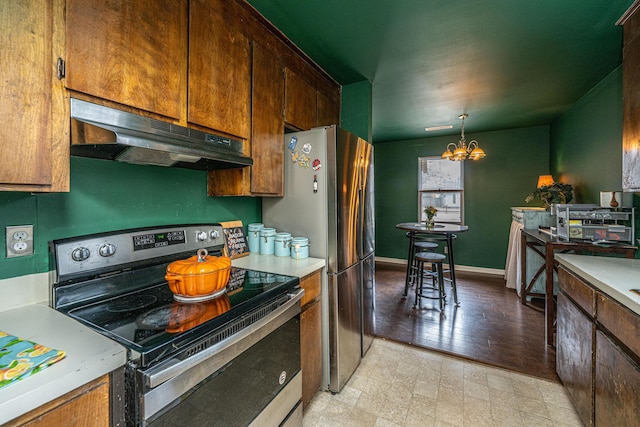 kitchen with appliances with stainless steel finishes, light countertops, a notable chandelier, and under cabinet range hood