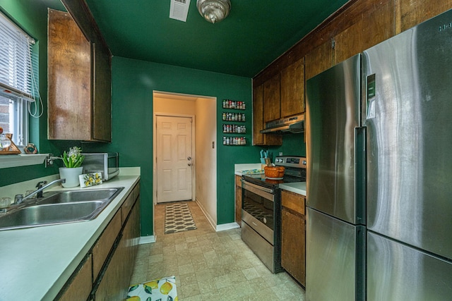 kitchen with light countertops, appliances with stainless steel finishes, a sink, and under cabinet range hood