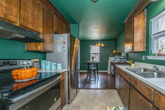 kitchen with light countertops, electric range, an inviting chandelier, a sink, and under cabinet range hood