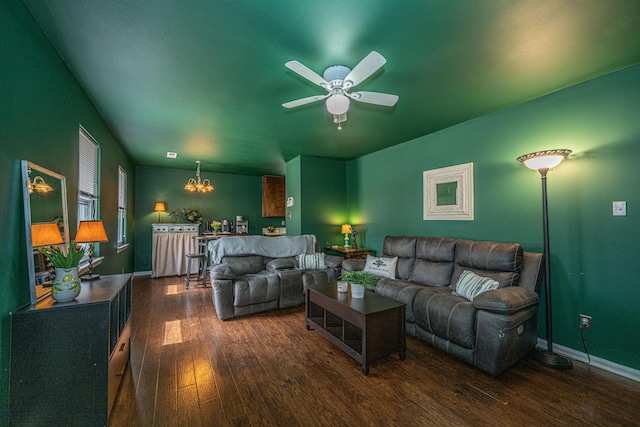 living room featuring dark wood-type flooring, baseboards, and ceiling fan with notable chandelier