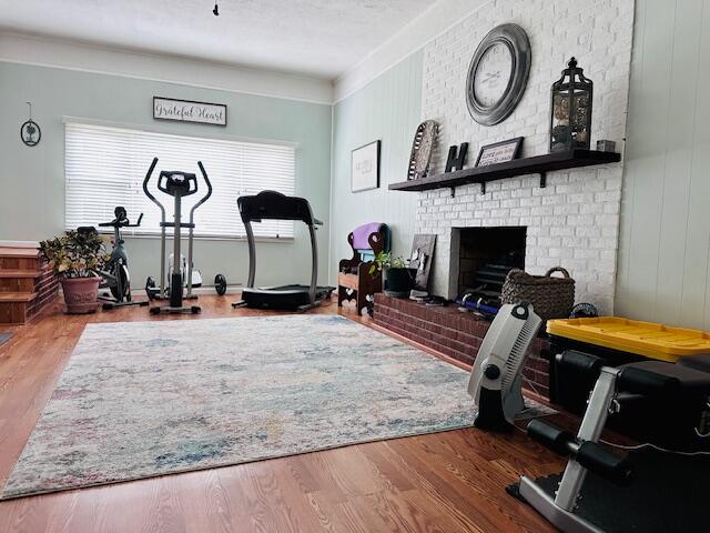 workout area featuring wood-type flooring, ornamental molding, and a brick fireplace