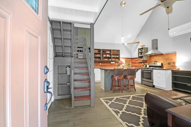 kitchen featuring gas stove, a breakfast bar, open shelves, beamed ceiling, and wall chimney exhaust hood