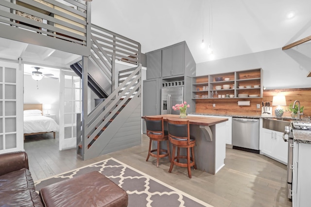 kitchen featuring light wood-style flooring, open shelves, a kitchen breakfast bar, stainless steel appliances, and butcher block counters