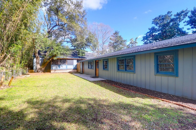 exterior space featuring board and batten siding, a shingled roof, a yard, and fence